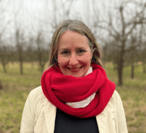 Christiane Herberth mit rotem Schal und weißer Jacke vor Obstbäumen im Winter